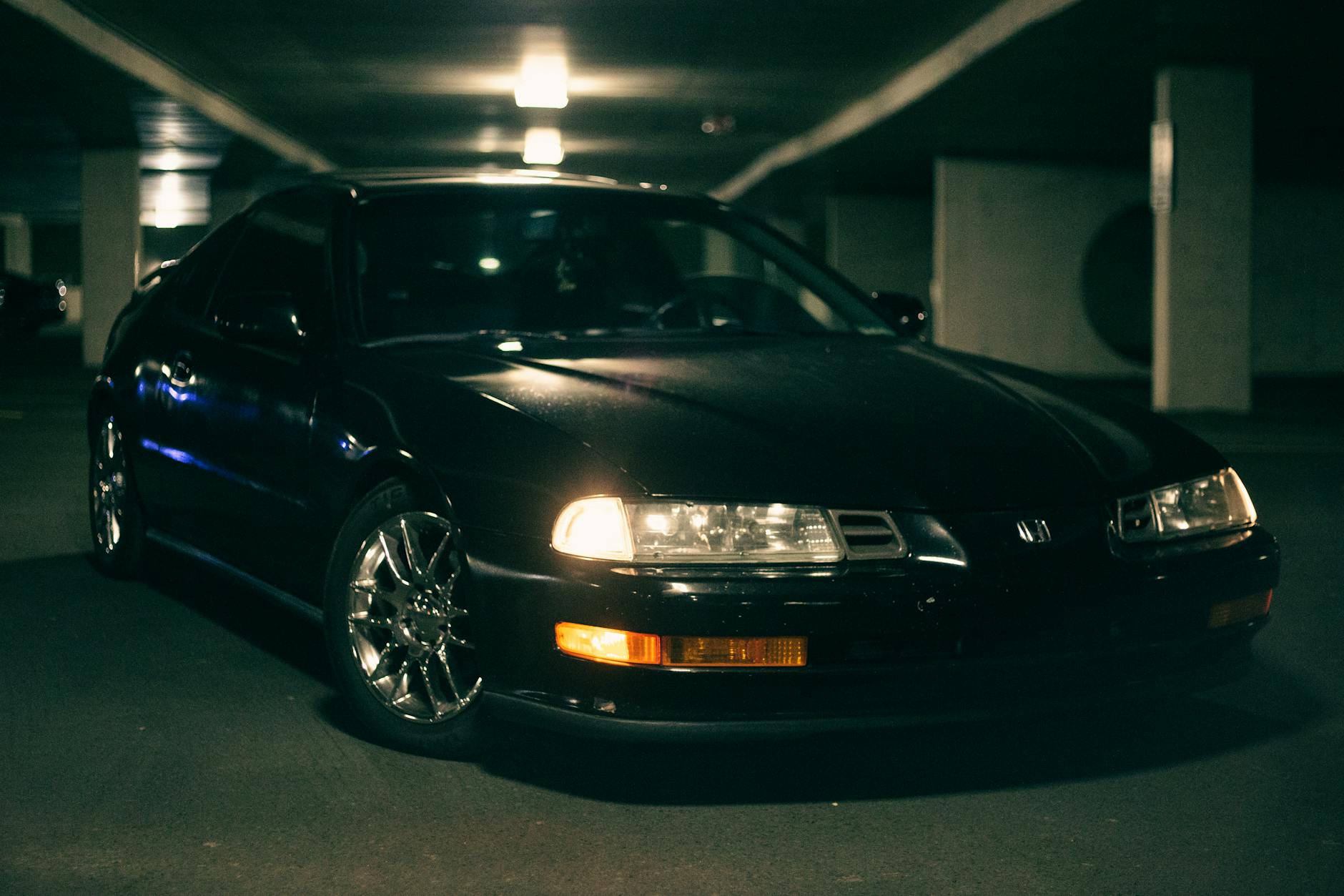 A black Honda car with headlights on, parked in an indoor garage, showcasing sleek design.